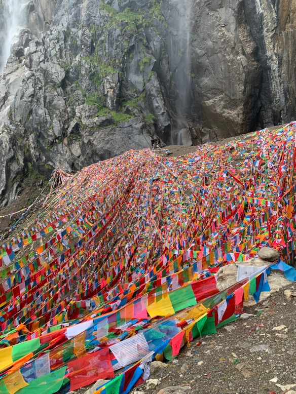 thousands of prayer flags on the rocks below the waterfall