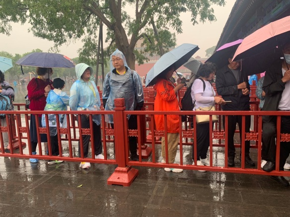 people in rain ponchos and holding umbrellas waiting in line