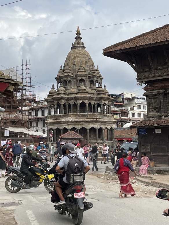 busy street scene with scooters and pedestrians making their way in front of a round temple