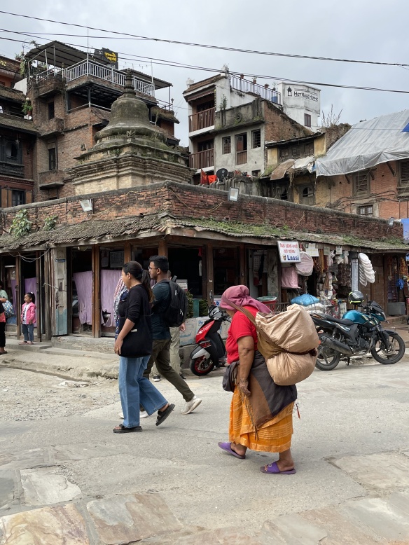 Kathmandu street with older woman carrying a large sack strapped to her back