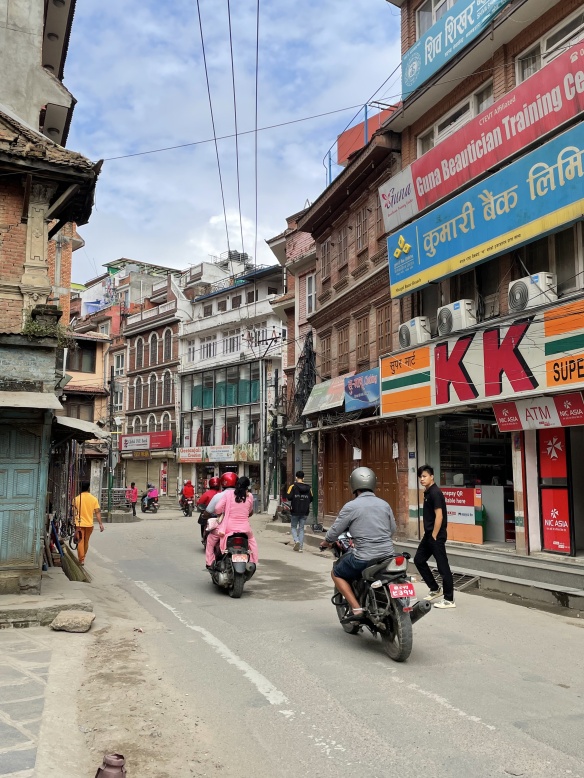 street scene with several scooters driving past "KK" market