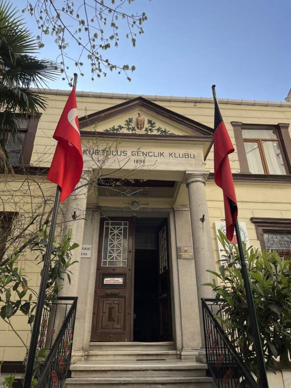 Official building with entrance flanked by Turkish flags and an inscription over the door: Kurtuluş Genclik Klubu